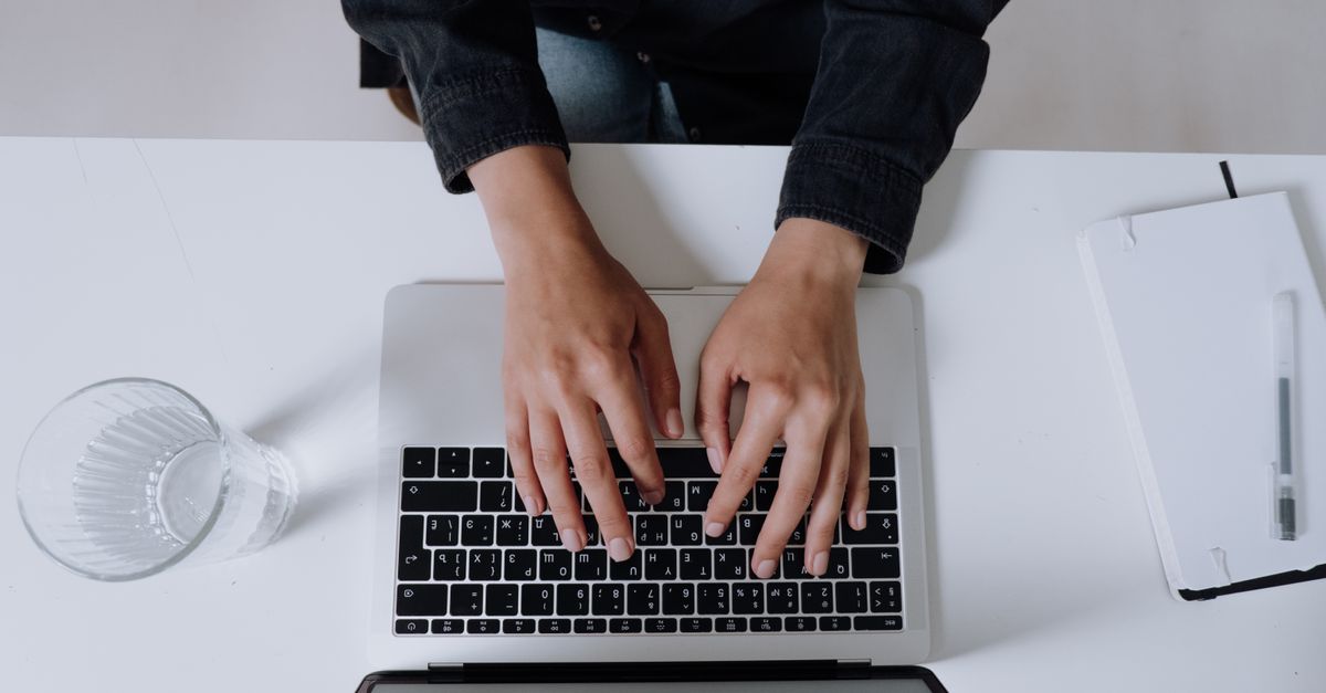 A person writing a blog post on a laptop with notes about length beside them.